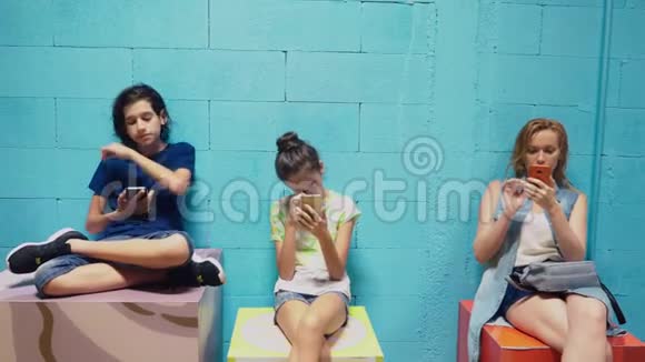 男孩女孩和女人坐在蓝色的墙上用手机视频的预览图