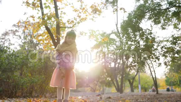 秋天公园里美丽的小女孩跳起来在背光下扔出黄叶视频的预览图