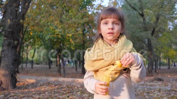 快乐的小女孩吹着泡泡在公园的背景树上微笑视频的预览图