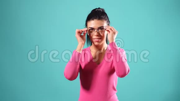 蓝色背景下穿戴眼镜和粉色连衣裙的布鲁内特模特的美画像完美的女孩在工作室里唱歌视频的预览图