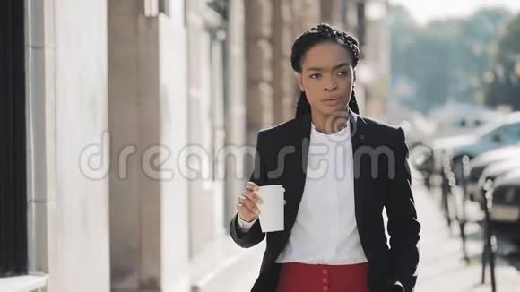 一个严肃的非洲裔美国女商人穿着西装在城市里走来走去喝着咖啡的肖像概念视频的预览图