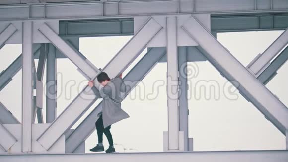 穿着灰色外套的年轻人爬上桥跨视频的预览图
