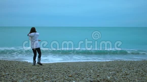 年轻女子把鹅卵石抛到海里泡沫般的波浪缓慢地溅上岸视频的预览图