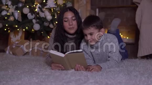 在圣诞节妈妈给儿子读了一本书吻了他躺在圣诞树附近的地板上高清高清视频的预览图