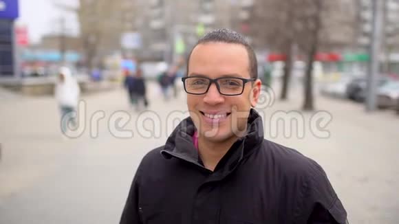 年轻快乐男子的肖像戴着眼镜看着相机在城市背景上微笑特写肖像画视频的预览图