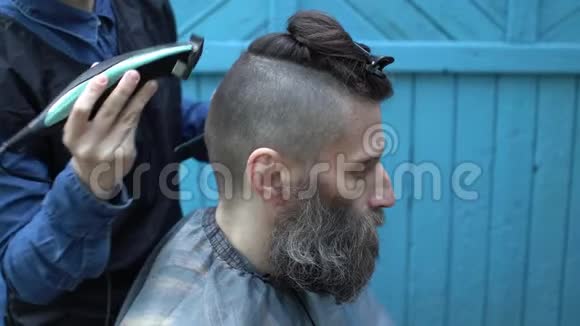 女理发师为中年男子理发户外用电动剃须刀和梳子视频的预览图