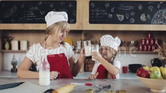 这位迷人的母亲和她漂亮的小女儿坐在厨房里喝牛奶的肖像画室内视频的预览图
