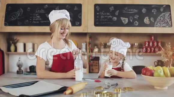 这位迷人的母亲和她漂亮的小女儿坐在厨房里喝牛奶的肖像画室内视频的预览图