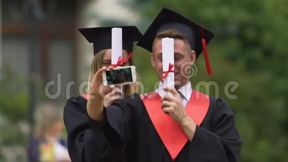 戴着学术帽和礼服的快乐男女在智能手机上拍摄视频视频的预览图