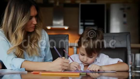 美丽的妈妈帮助她的儿子用彩色铅笔画图像帮助培养孩子想象力视频的预览图