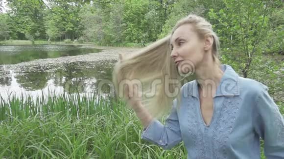 那个年轻的女人在湖的背景下梳着一头长发慢动作视频的预览图