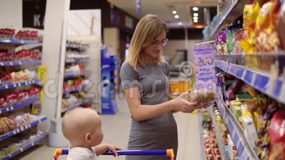 年轻的母亲正在阅读饼干包装上的产品内容微笑着而她的小婴儿正坐在一个视频的预览图