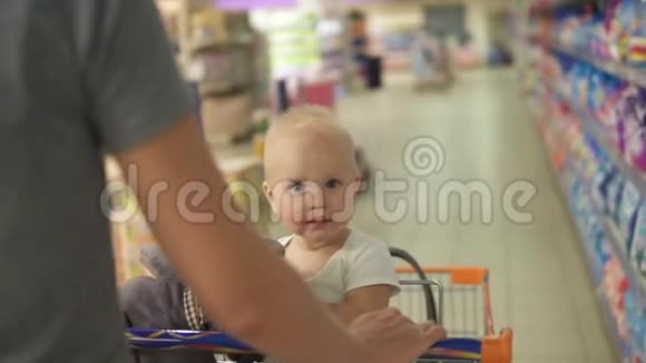 小宝宝坐在超市里的一辆购物车里手里拿着一个玩具而她的妈妈正在推着手推车走在中间视频的预览图
