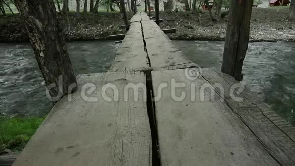 女人的腿沿着一座狭窄的木桥走在一条山河上野营和冒险概念视频的预览图