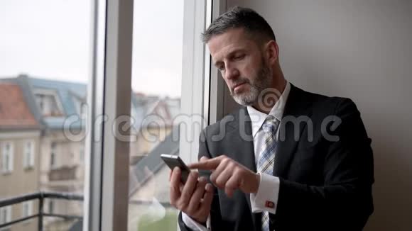商人站在窗边在手机上写字的照片视频的预览图