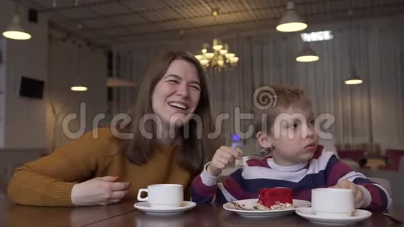 有趣的小男孩和美丽的年轻母亲喝茶吃蛋糕视频的预览图