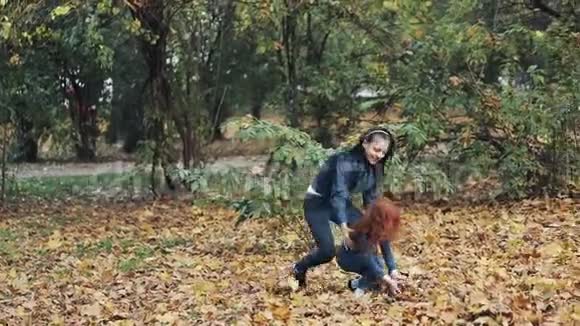 快乐的母亲和她的小女儿在秋天公园玩得很开心年轻的家庭扔树叶笑慢动作视频的预览图