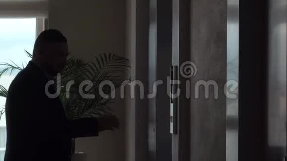 男子按按钮在公寓走廊呼叫电梯使用手机视频的预览图