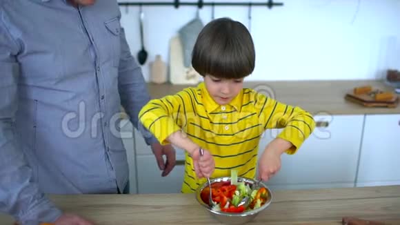 小有趣的男孩坐在厨房里玩他父亲刚准备的蔬菜沙拉父亲节视频的预览图