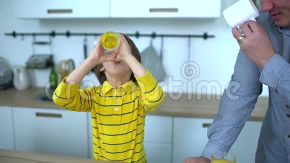 父亲和非常可爱的男孩在厨房里喝橙汁健康的生活方式父亲节慢动作视频的预览图