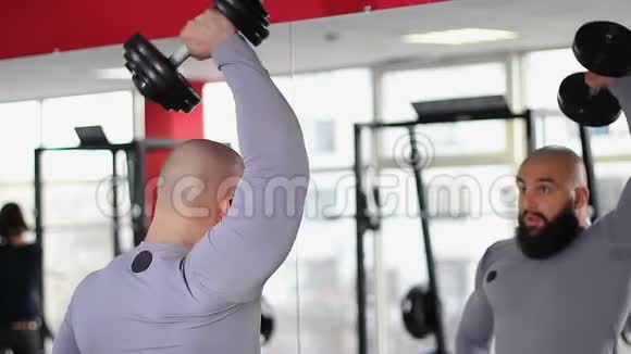 男运动员在体育馆镜前用哑铃做运动视频的预览图