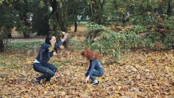 快乐的母亲和她的小女儿在秋天公园玩得很开心年轻的家庭扔树叶笑慢动作视频的预览图
