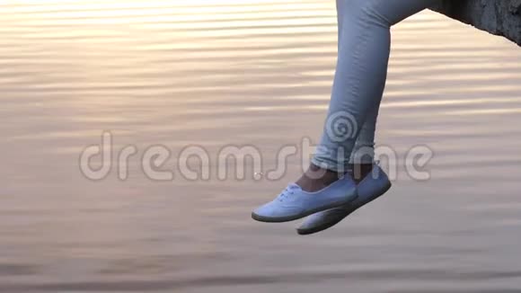 穿着白色鞋子的女人的腿在平静的水面上晃荡视频的预览图