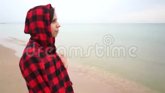 海滩上一个戴着兜帽的女孩沉思地看着远处视频的预览图