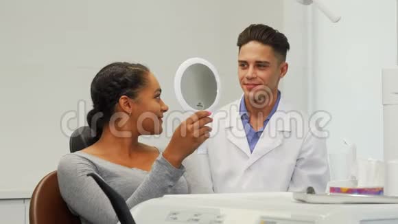 美丽的女人在牙科诊所照镜子检查她的笑容视频的预览图