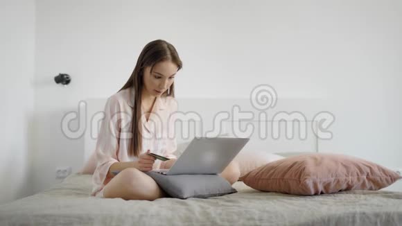 漂亮的女人正在床上的笔记本电脑上网上购物视频的预览图