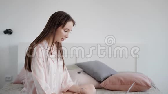 可爱美丽的黑发女孩坐在床上穿着丝绸长袍视频的预览图