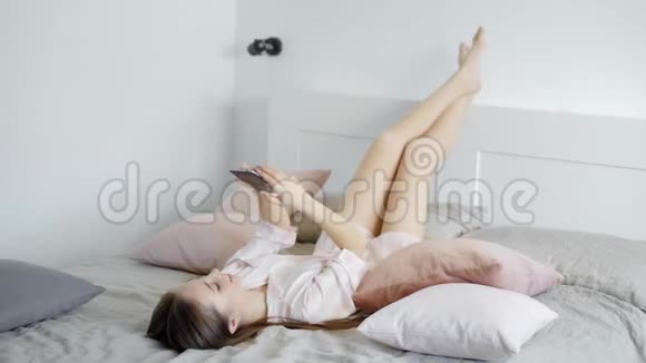 美丽的年轻黑发女孩躺在床上穿着浅色的丝绸长袍视频的预览图