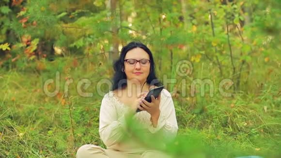 森林里一个戴眼镜的年轻女子坐在草地上用信使传达信息视频的预览图