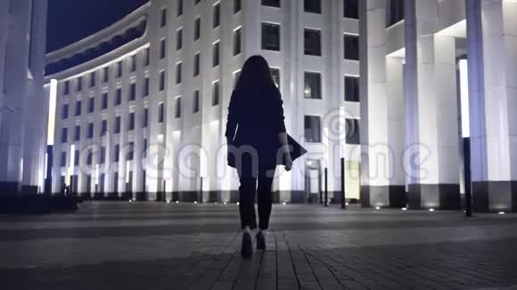 一位年轻女商人走在夜市街道上的后视图视频的预览图