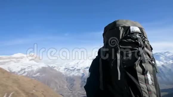 一个长胡子的人戴着太阳镜帽子背着背包和照相机站在山上看着场边视频的预览图