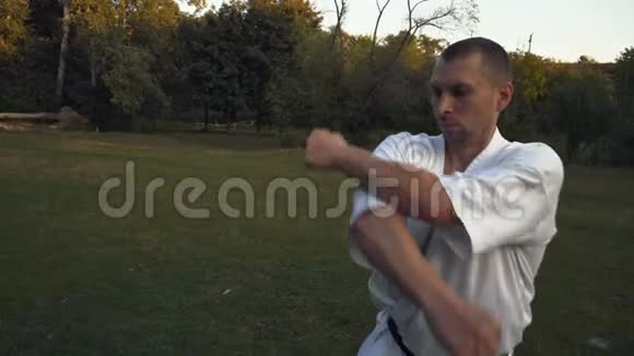 空手道练习者一个穿着白色和服的男人在城市公园的空地上做健身气功表演视频的预览图
