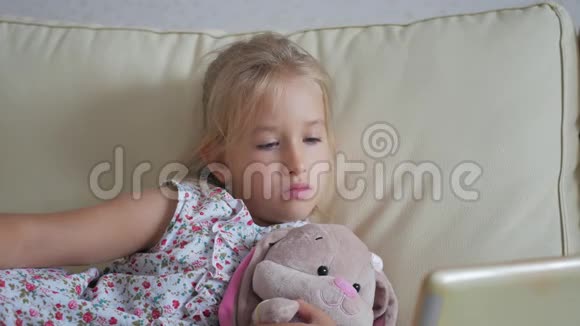 可爱的女孩和她最喜欢的玩具是一只毛绒兔子家里有平板电脑视频的预览图