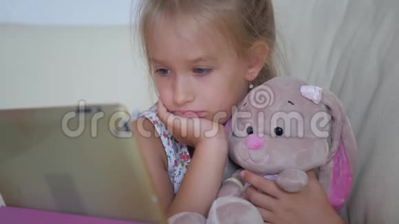 可爱的女孩和她最喜欢的玩具是一只毛绒兔子家里有平板电脑视频的预览图