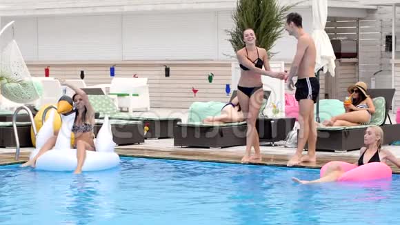 游泳池边休息积极的男人和女孩牵着手缓慢地跳进游泳池视频的预览图