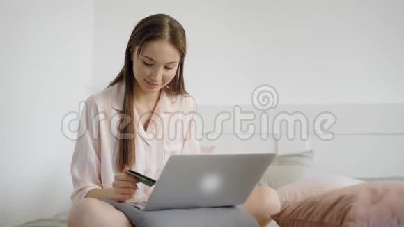 女孩正在网上买东西坐在家里的床上把她的信用卡数据放在网上前台查看视频的预览图