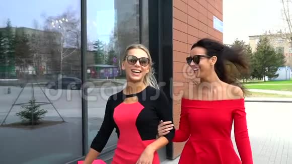 年轻的女朋友在购物的一天笑着穿着红色裙子的快乐女人在城市大街上散步和交谈视频的预览图