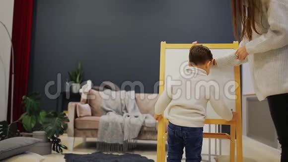小男孩和妈妈在她的客厅房子油漆板上的标记一个孩子画休闲幸福家庭视频的预览图