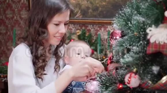 一位年轻的母亲和一个小儿子在壁炉附近的房间里打扮一棵圣诞树视频的预览图