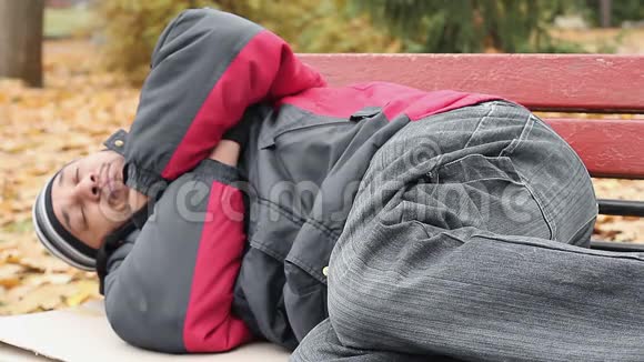穿着夹克和牛仔裤的瓦加邦德睡在长凳上试图保暖贫穷视频的预览图