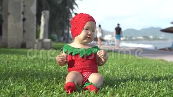 穿着草莓服装的特写亚洲女婴在海滩上吃饼干视频的预览图
