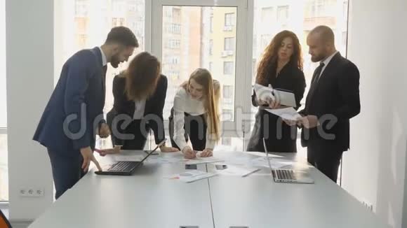 办公室工作人员站在一张桌子旁讨论公司的财务问题一支由三名妇女和两名男子组成的年轻团队视频的预览图