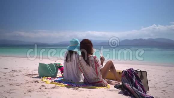 两个漂亮的女孩在海滩上完美地休息喝着粉红色的沙子香槟看看热带的蔚蓝水域视频的预览图