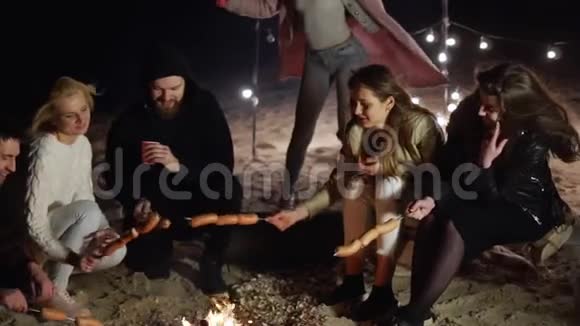 晚上在海滩篝火旁用香肠和饮料野餐年轻人视频的预览图