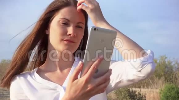 女人用手机对抗蓝天微笑女性慢动作在手机上自拍视频的预览图