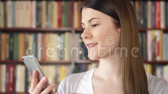 女大学生在大学图书馆使用手机浏览阅读与朋友聊天视频的预览图